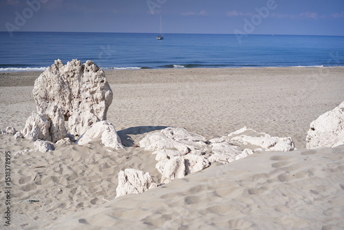 Fototapeta Naklejka Na Ścianę i Meble -  Tranquil beach with rocky shoreline and sailboat on serene horizon. Patara Beach in Turkey
