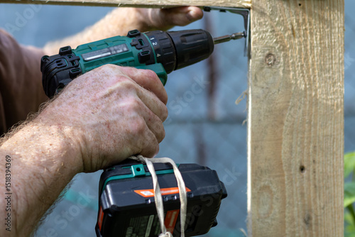 Obraz na płótnie Hands of man using drill to assemble wooden structure. Close-up.