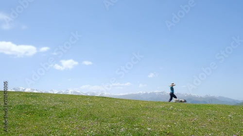 Woman fooling around and running with her dog in a flower meadow against the backdrop of snowy mountains in spring. Cheerful atmosphere of rest and relaxation in nature