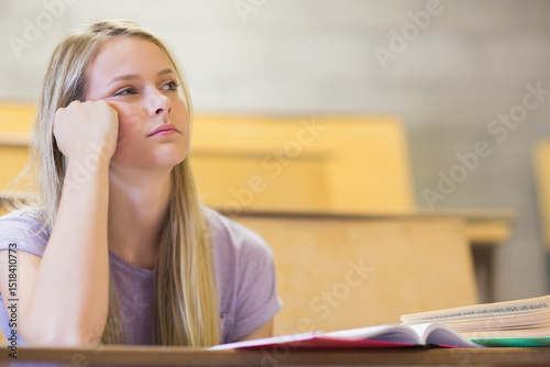 Teenage female student in purple T-shirt looking aside at open textbook on lecture desk, copy space