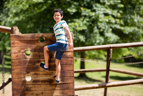 Female child climbing wooden panel with round holes at park playground near chain links, copy space
