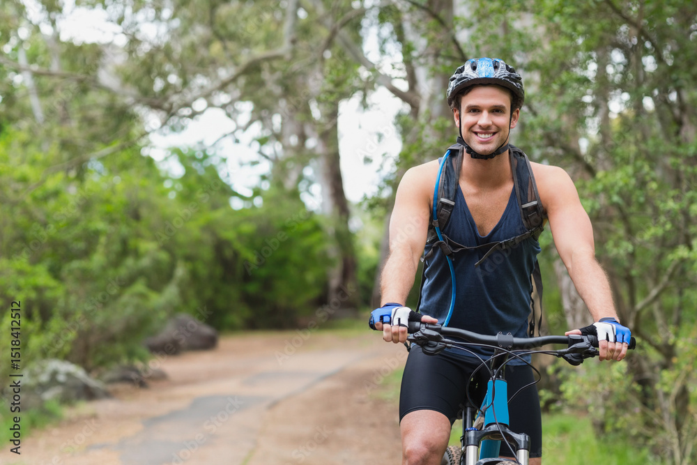 Naklejka premium Man riding mountain bike on dirt trail in forest wearing cycling helmet and hydration backpack
