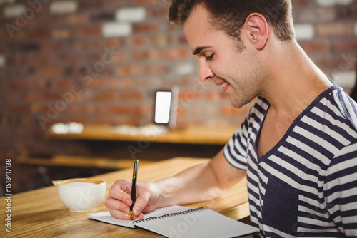 Man writing in notebook with pen at brick-walled cafe table with coffee cup, copy space