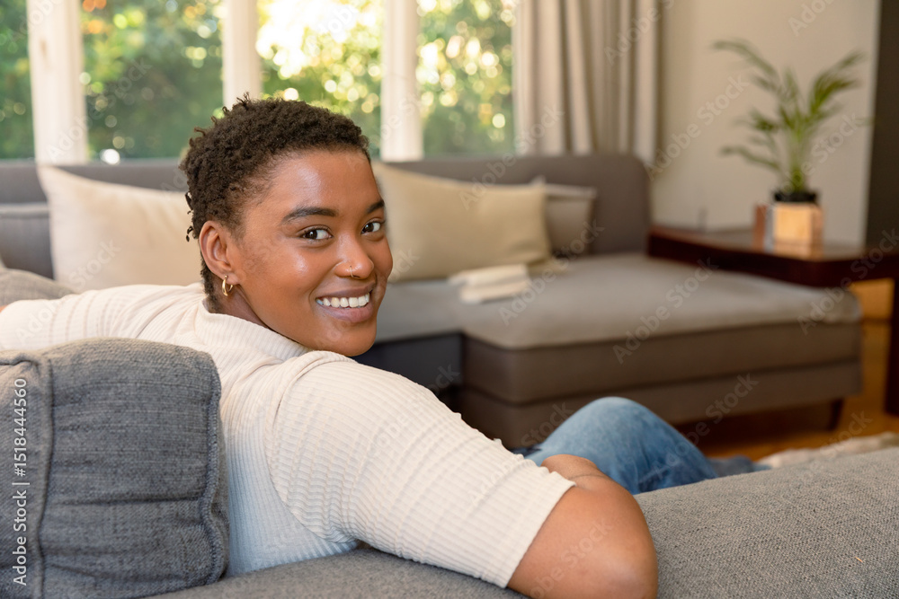 African American adult woman reclining on grey sofa by tall windows at home with folded book African American adult woman reclining on grey sofa by tall windows at home with folded book