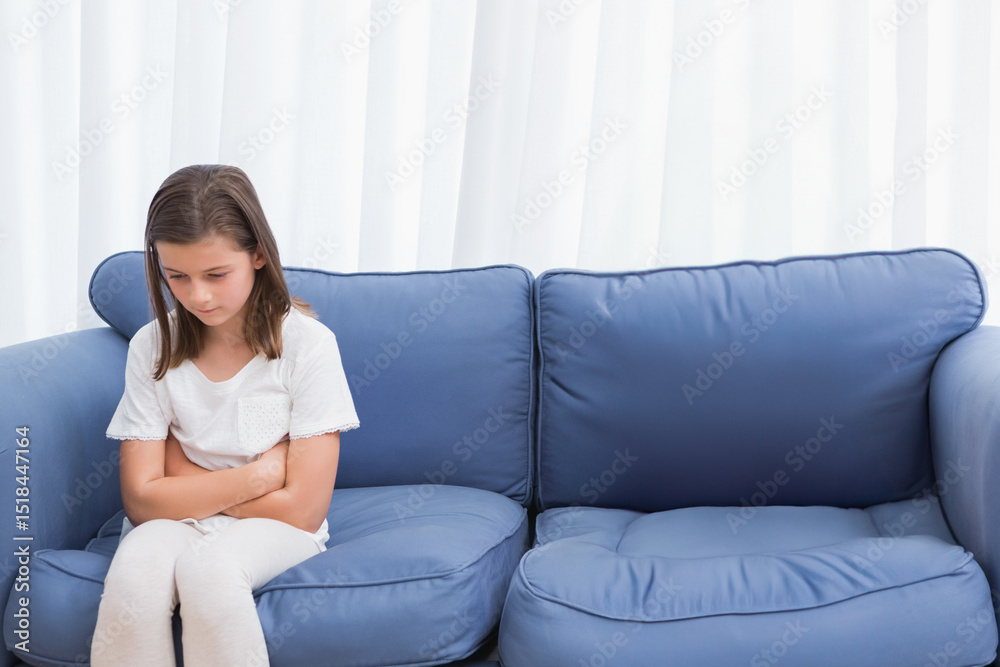 Female child sitting on blue sofa with cushions in living room near white curtains, copy space Female child sitting on blue sofa with cushions in living room near white curtains, copy space