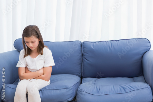 Female child sitting on blue sofa with cushions in living room near white curtains, copy space