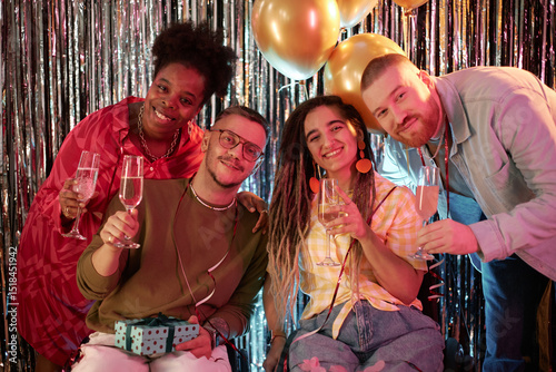 Diverse group of young adults celebrating birthday, smiling and holding champagne glasses, two people sitting in wheelchairs with disability, festive balloons and decorations in background photo