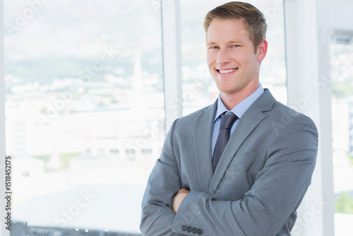 Corporate executive standing with arms crossed before floor-to-ceiling windows showing city skyline
