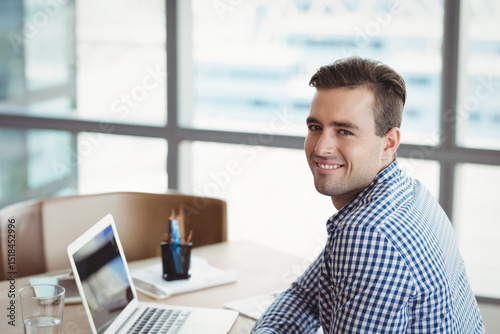 Adult man working at desk in bright modern office with laptop and notebook, copy space