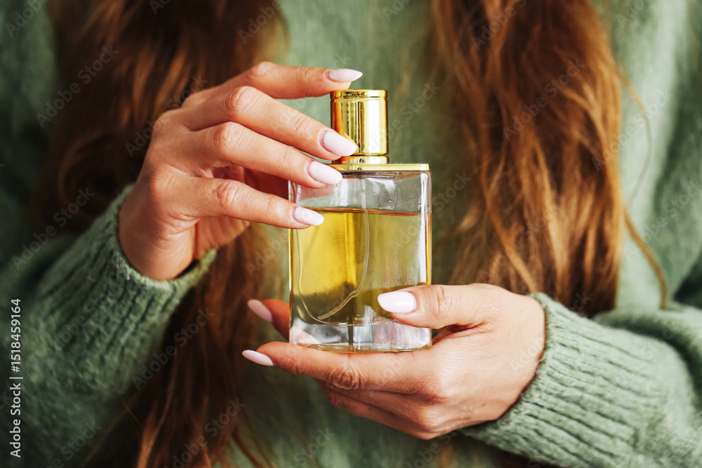 Fototapeta premium Woman holding perfume bottle. Golden fragrance in elegant flacon. Close-up hands and long hair. Personal care routine. Luxury beauty product. Feminine style accessory. Glamour and elegance detail.