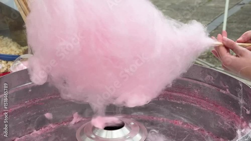 A large fluffy pink cotton candy is being spun on a stick inside a cotton candy machine