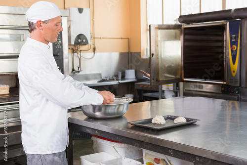 Bowl mixing dough in bakery on countertop with tray holding dough balls near industrial ovens