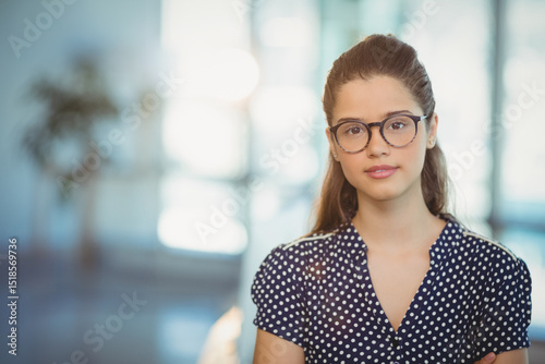 Woman wearing eyeglasses and navy polka-dot blouse standing in coworking space with potted plant