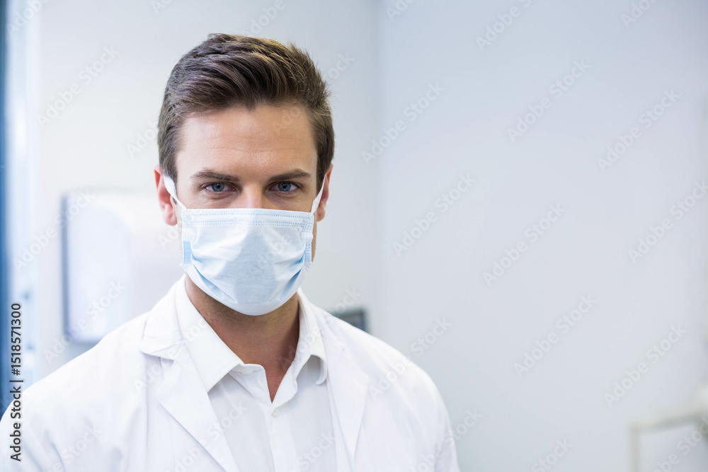 White male healthcare worker standing in clinic wearing lab coat and mask with dispenser, monitor White male healthcare worker standing in clinic wearing lab coat and mask with dispenser, monitor