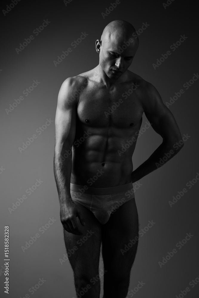 Fototapeta premium Black and white image of a muscular man posing gracefully, showcasing strength, confidence, and vulnerability in a simple yet captivating composition.