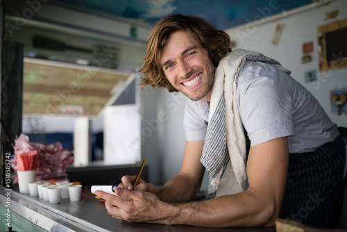 Billede på lærred Male concession worker in apron leaning over counter at food truck, writing on n