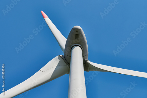 Close up view of wind turbine with red tipped blades set against clear, vibrant blue sky on sunny day, evoking clarity and commitment to environmental sustainability