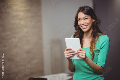 Asian woman smiling and holding white tablet at home office with documents on table, copy space
