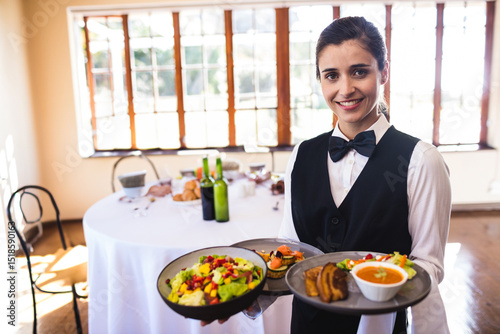 Female server holding trays laden with salad soup bread appetizers in banquet hall, copy space