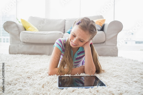 Girl lying on white shag carpet in front of gray sofa with colorful pillows using tablet
