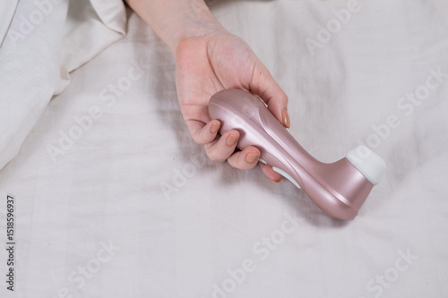 Woman lying in bed holding clitoral vacuum vibrator. 