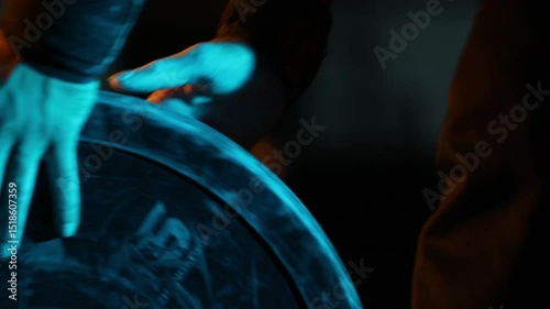 Close-up of an athlete's hands with wrist wraps grabbing a heavy weight plate. Dramatic blue and warm lighting creates a powerful, focused, and cinematic training atmosphere.