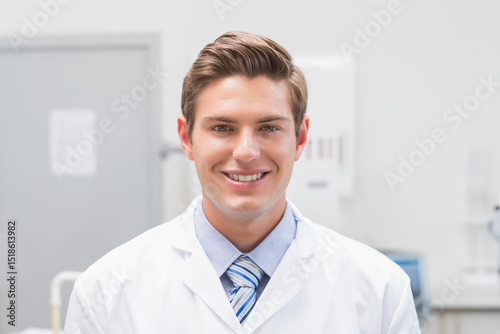 Male doctor smiling while wearing white lab coat and striped tie in clinic room with dispenser