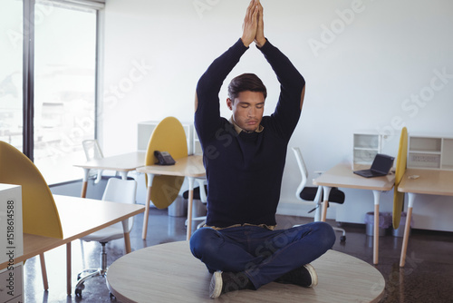 Pacific Islander man wearing navy sweater meditating on round table in open-plan office with laptop