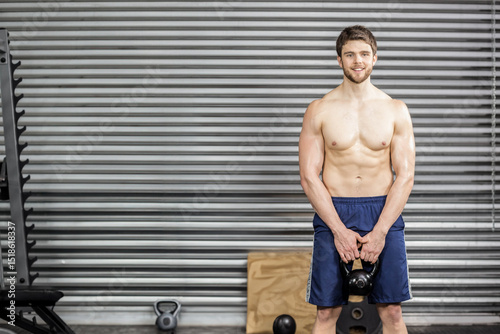 Man gripping kettlebell at thigh level in gym with weight rack, plyometric box, copy space