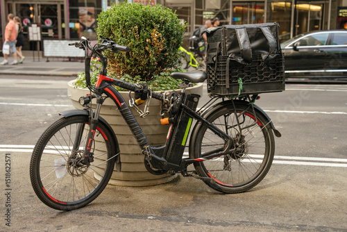Wallpaper Mural An electric delivery bicycle with a large rear cargo box is parked near a planter on a busy New York street. The scene reflects urban life, gig economy work, and eco-friendly transportation. Torontodigital.ca