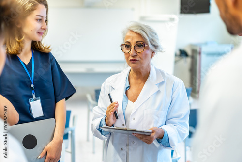 Wall Mural Senior doctor leading medical briefing with clipboard and pen in hospital confer