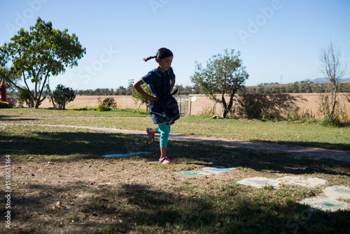Obraz na plátně African American girl hopping over painted hopscotch squares on grass in rural p