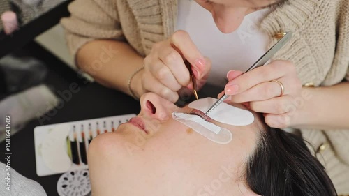 Cosmetologist girl glues and separates eyelashes with tweezers.