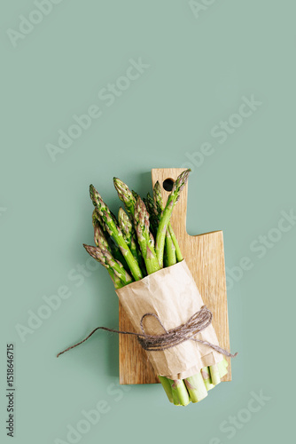 Organic green asparagus in paper wrap placed on a wooden board with soft green background