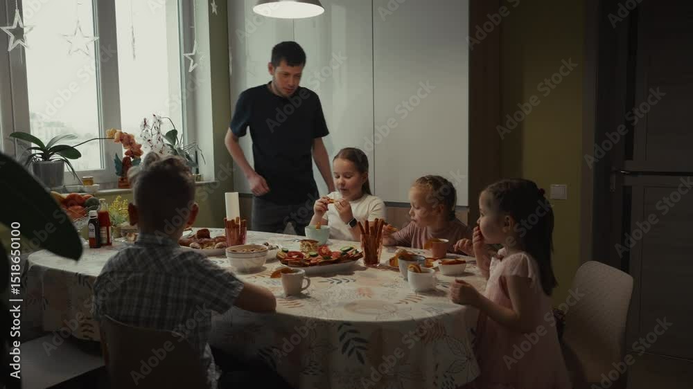 Family enjoys meal together at home. Father serves food to children. Family enjoys meal together at home. Father serves food to children.