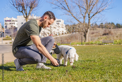 Man picking up dog poop with retractable leash in park photo