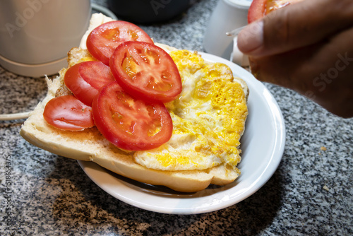 An open bread with mayonnaise, many well-arranged tomato slices and a fried egg, in the blur in the upper right corner there is a hand slicing the tomato