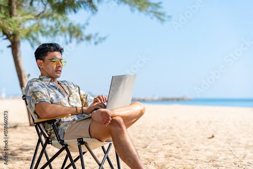 Asian man remote working corporate business on laptop computer while travel the sea on summer beach holiday vacation. Workation, work from anywhere with wireless technology and digital gadget device.