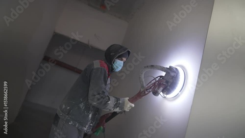 Masked worker skillfully operates grinding machine against rough plaster. Vigorous precise and safe technique refines wall texture