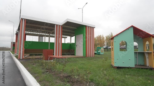 Colorful pavilion with benches stands amidst kindergarten yard. Canopy and cheerful seating invite outdoor play along with socialization