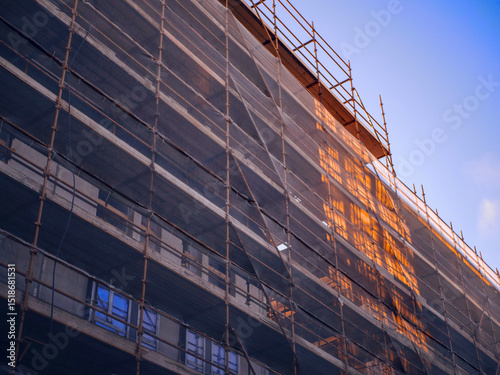 A construction site with scaffolding on a building. The sky is blue. Teal and orange sun rise color. Residential house construction.