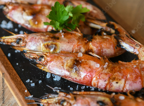 Grilled tiger prawns on a black plate with parsley