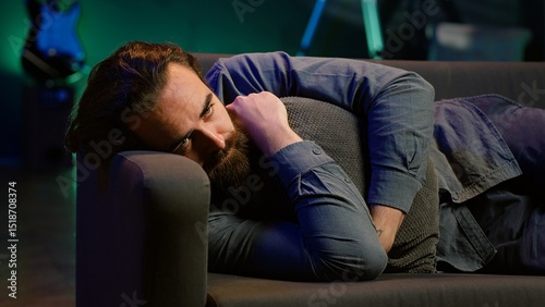 Man laying down hugging pillow watching TV, heartbroken by upsetting movie plot. Sad viewer lounged on couch in RGB illuminated apartment, upset by depressing television show scene, camera A