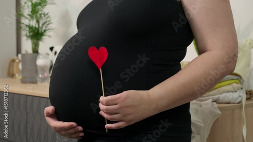 Pregnant woman holding red heart shape and feel love for unborn baby in belly. Awaiting for baby. Concept of maternity and pregnancy care