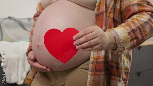 Pregnant woman holding red heart shape and feel love for unborn baby in belly. Awaiting for baby. Concept of maternity and pregnancy care