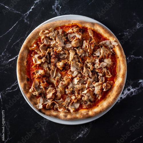 Top view of a pizza with kebab meat, placed on a black marble surface.