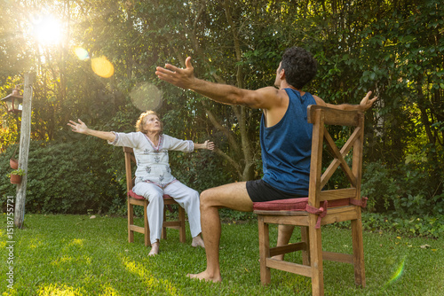 Fototapeta Senior woman and physiotherapist doing seated exercises outdoors