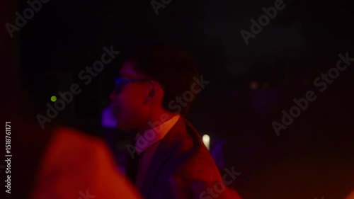 Close up of man in a suit wearing glowing blue LED glasses dances at a nighttime party, illuminated by vibrant neon lights. Concept of event, nightlife, celebration, and entertainment themes