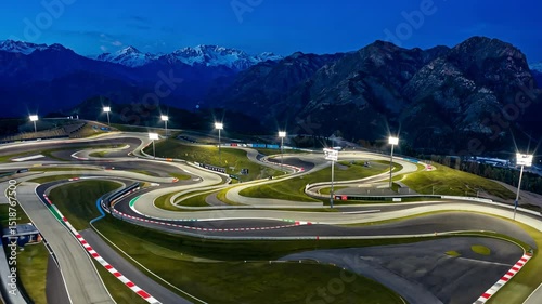Winding race track illuminated at night, with mountains in the background and bright lights along the track. motion video.
