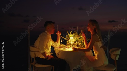 Rising a glass of champagne during a romantic candlelit dinner. Asian man and woman at their date on the outdoor terrace of restaurant. 
